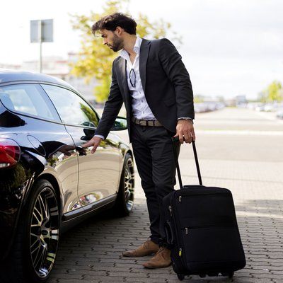 A man with a suitcase opening a car door