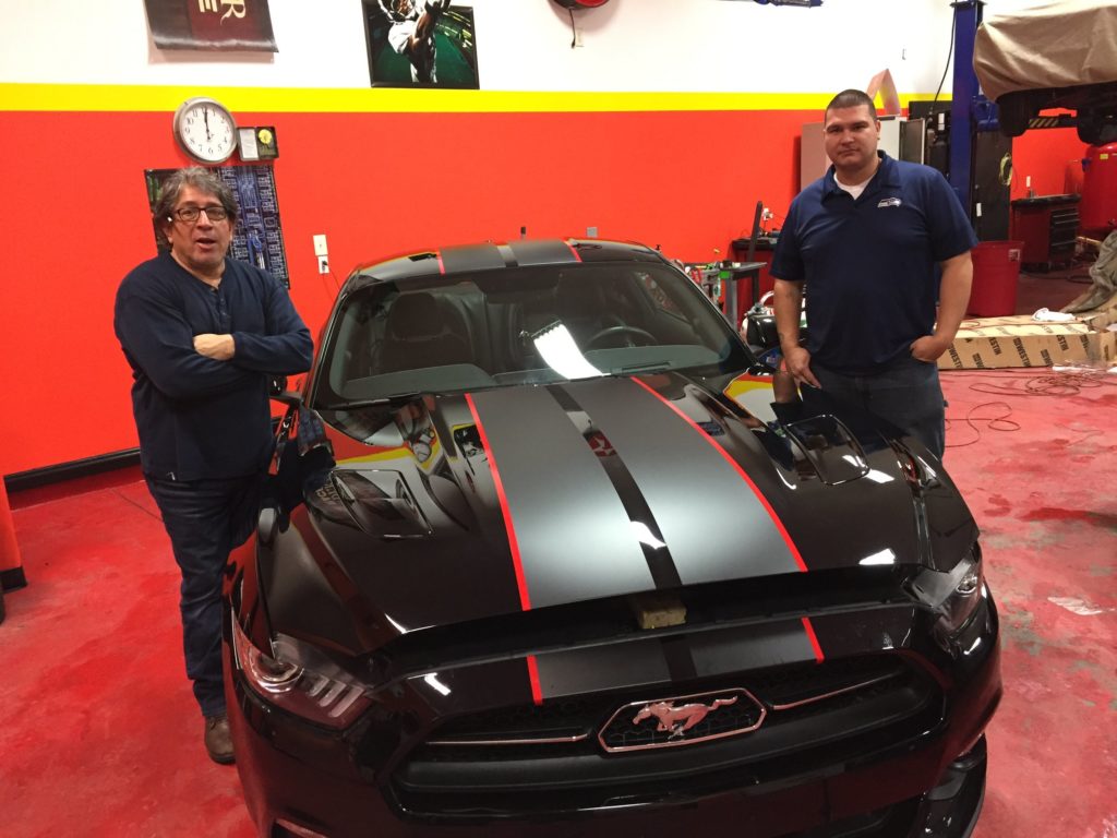 Two guys posing with a black Mustang